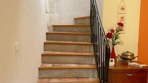 Una escalera con escalones de madera y barandilla metálica, que conduce a una plataforma con un armario de madera y un florero.
