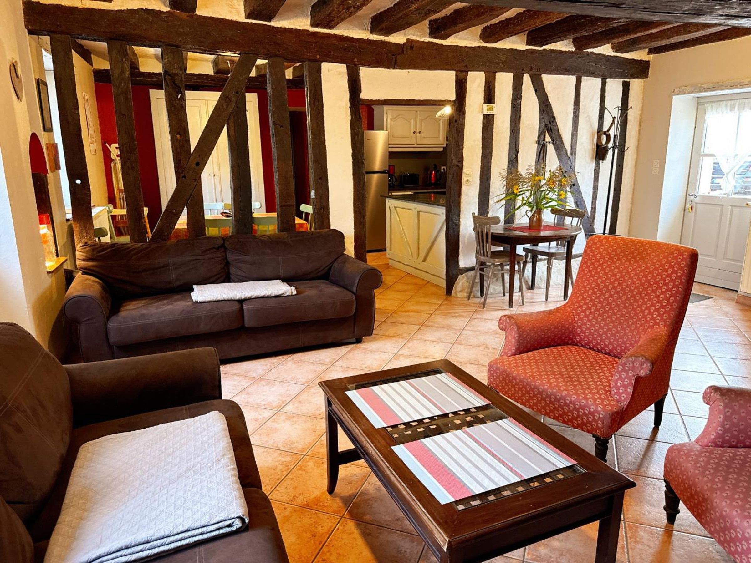 Una sala de estar acogedora con un sofá, un sillón y una mesita de centro. Se observa una cocina al fondo con una mesa de comedor y sillas.