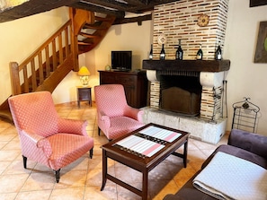 A cozy living room with a fireplace, two patterned armchairs, a wooden coffee table, and a staircase.