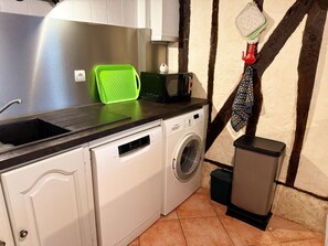 Una cocina compacta con lavadora Bosch, un escurreplatos verde, microondas y cubo de basura.