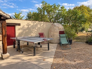 Una mesa de ping pong con una silla roja, un sillón verde y una estructura de piedra en un jardín.