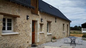 Un bâtiment en pierre doté d’une terrasse carrelée, d’une porte en bois et d’un petit jardin avec une table et des chaises.