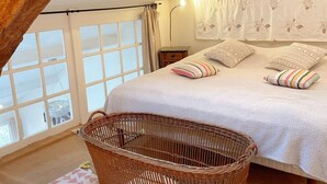 A bedroom with a large bed, a wicker basket, and a window with curtains.
