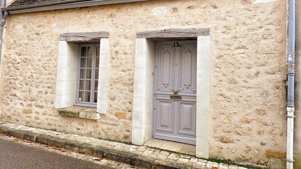 A building with a textured stone facade, a window with a white frame, and a door with a white frame and a brass knocker.