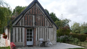 Une maison traditionnelle à colombages, avec une façade en briques, une porte blanche et un petit jardin agrémenté d’une table et de chaises.