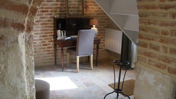 Ein Zimmer mit Backsteinwand, Schreibtisch mit Stuhl, Heizkörper und Bücherregal.