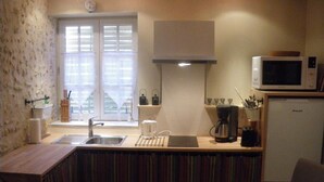 Eine kleine Küche mit Spüle, Kaffeemaschine, Mikrowelle und einem Fenster mit Jalousien.