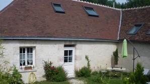Ein Haus mit geneigtem Dach, zwei Fenstern, einer Tür und einem kleinen Garten mit Tisch und Stuhl.