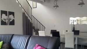 A modern living room with a black leather sofa, a staircase, and a dining area with white chairs and a table. - Modern house with large heated pool and pets allowed (Averdon)