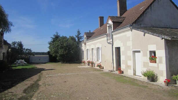 A two-story building with a tiled roof, a gravel driveway, and potted plants.