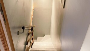 A narrow staircase with a handrail, leading to a landing with a light fixture.