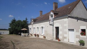 A two-story building with a tiled roof, a front door, and a small porch area with outdoor seating.