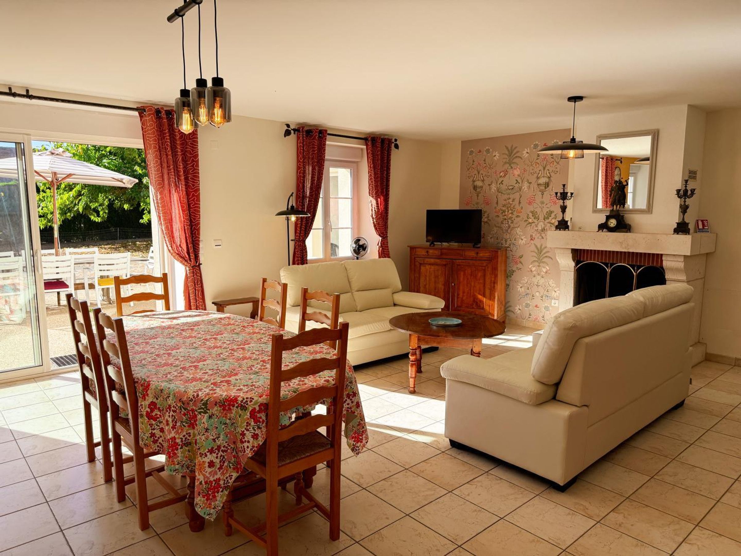 Een woonkamer met een bank, een eettafel met stoelen, een televisie op een houten kast en een open haard.