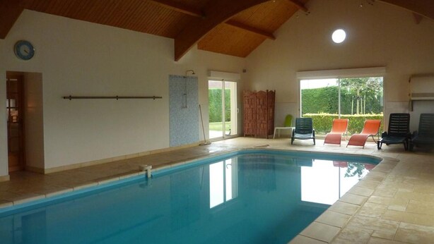 Una piscina interior con suelo de baldosas, techo de madera y vistas al exterior a través de amplios ventanales.