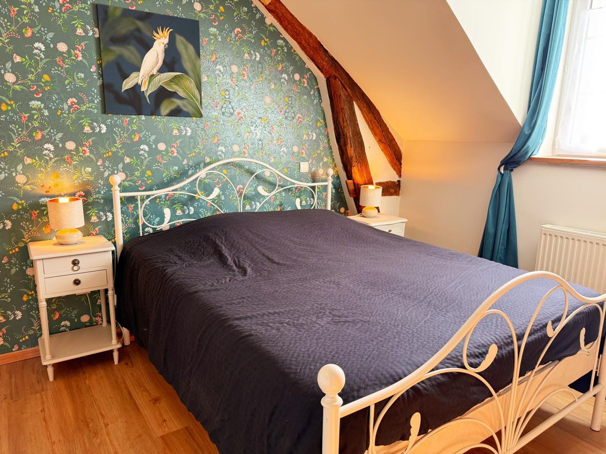 Een slaapkamer met een bed, twee nachtkastjes, een radiator, een wandlamp en een raam met gordijnen.