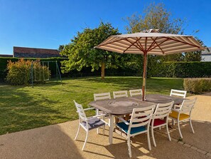 Une terrasse avec une table ronde et des chaises, un parasol et une balançoire dans un jardin.