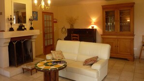 Una sala de estar con un sofá blanco, una mesa redonda de centro, una chimenea, un mueble de madera y una araña.