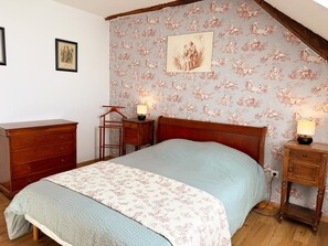 A bedroom with a bed, dresser, nightstand, and a wall with a floral wallpaper and a framed picture.