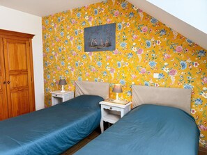 A bedroom with two single beds, a wooden wardrobe, a painting on the wall, and a floral wallpaper pattern.
