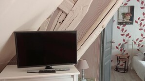 Un dormitorio con una televisión sobre un tocador blanco, una lámpara y una mesita con una silla.