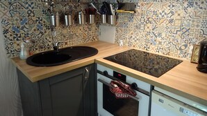 Una cocina con un lavamanos negro, estufa y microondas. Hay armarios y un salpicadero de azulejos.