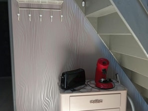 Una kitchenette pequeña con microondas, tostadora y cafetera roja sobre una encimera blanca.
