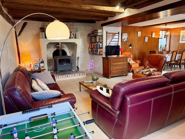 A cozy living room with a fireplace, leather furniture, a foosball table, and a dining area.
