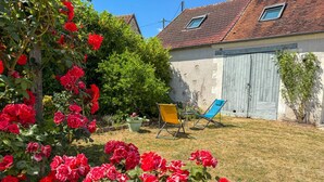 A garden with red roses, a blue chair, and a yellow chair in a backyard with a house in the background.