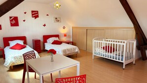 A room with two beds, a crib, a table, and a chair.