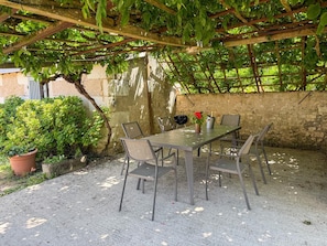 An outdoor patio with a table and chairs, surrounded by greenery and a stone wall. - Idyllic Family Retreat: Spacious Home with Garden, Kid-Friendly Amenities, and Nearby Attractions (Couddes)