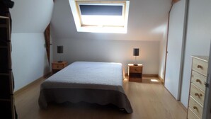 A bedroom with a skylight, a bed, two bedside tables, and a dresser.
