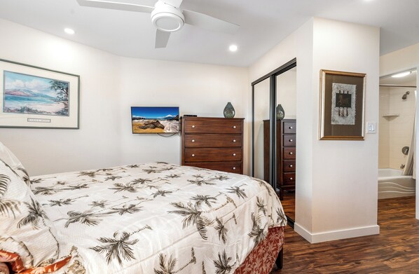 A bedroom with a bed, a dresser, a ceiling fan, and a bathroom visible through an open door.
