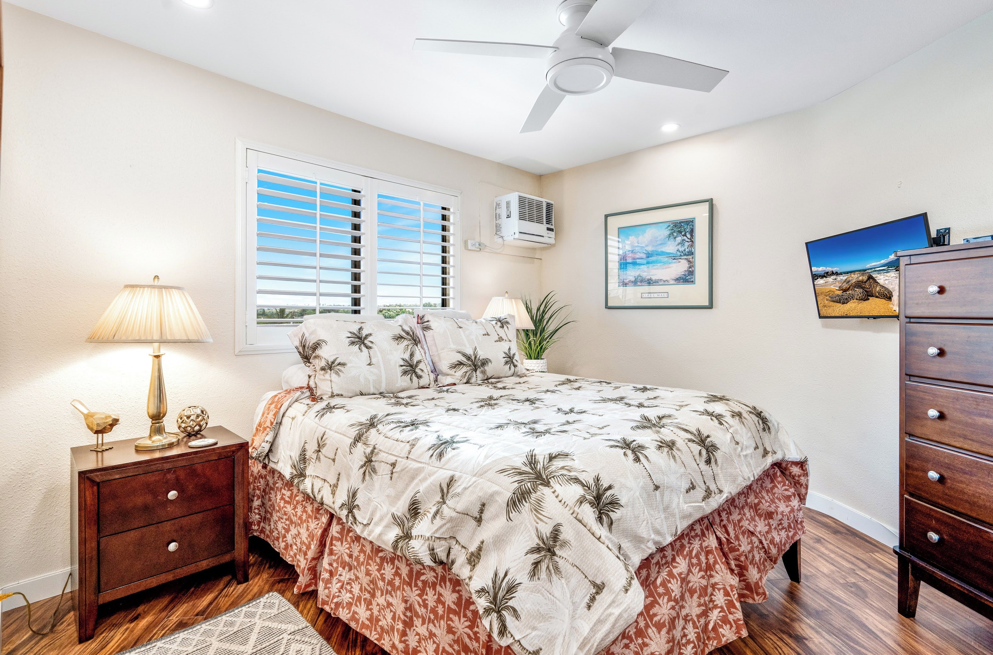 A bedroom with a bed, nightstand, dresser, ceiling fan, window with blinds, air conditioning unit, and wall art.