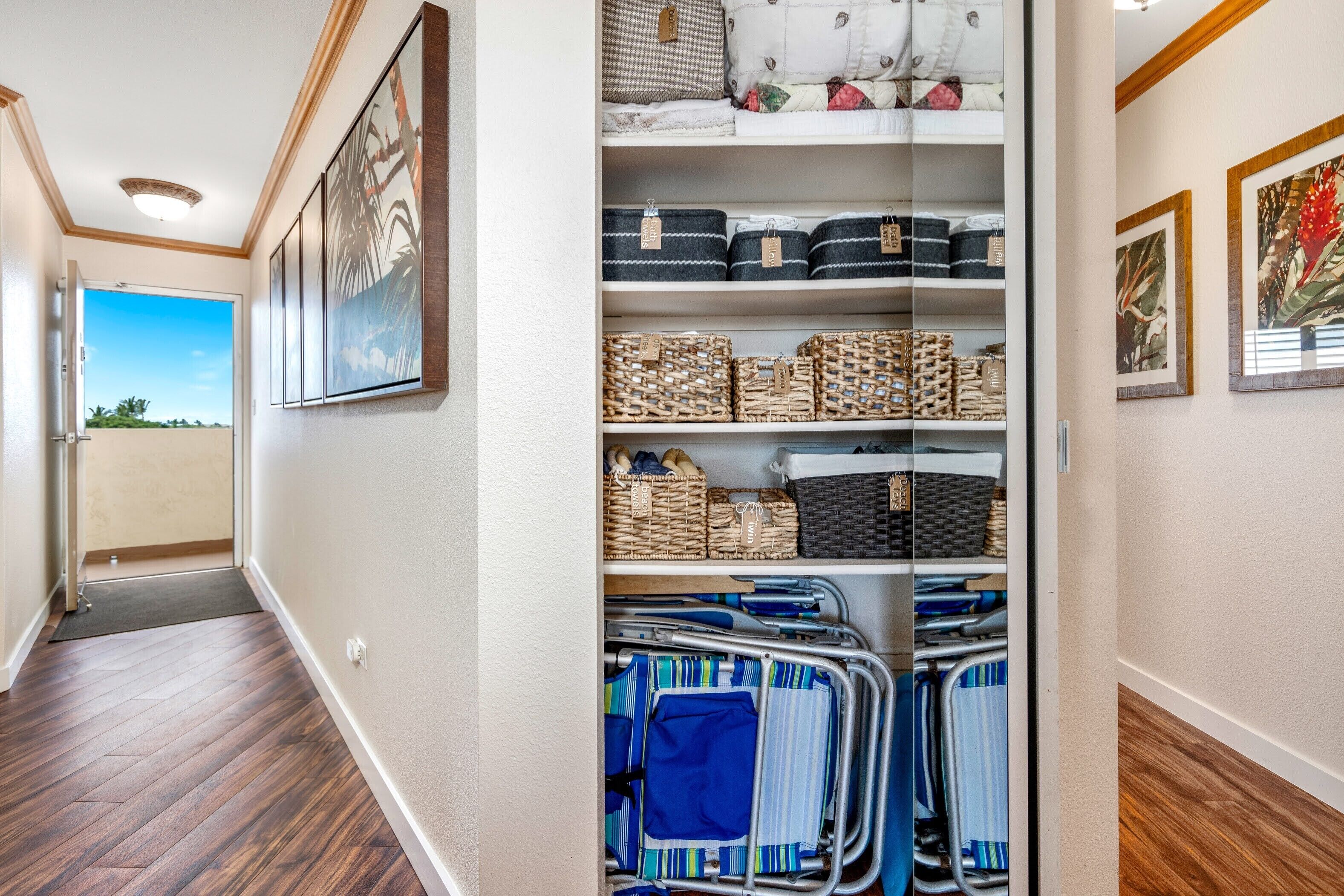 A hallway with a wooden floor, a door leading outside, and a storage unit with baskets and folded clothes.