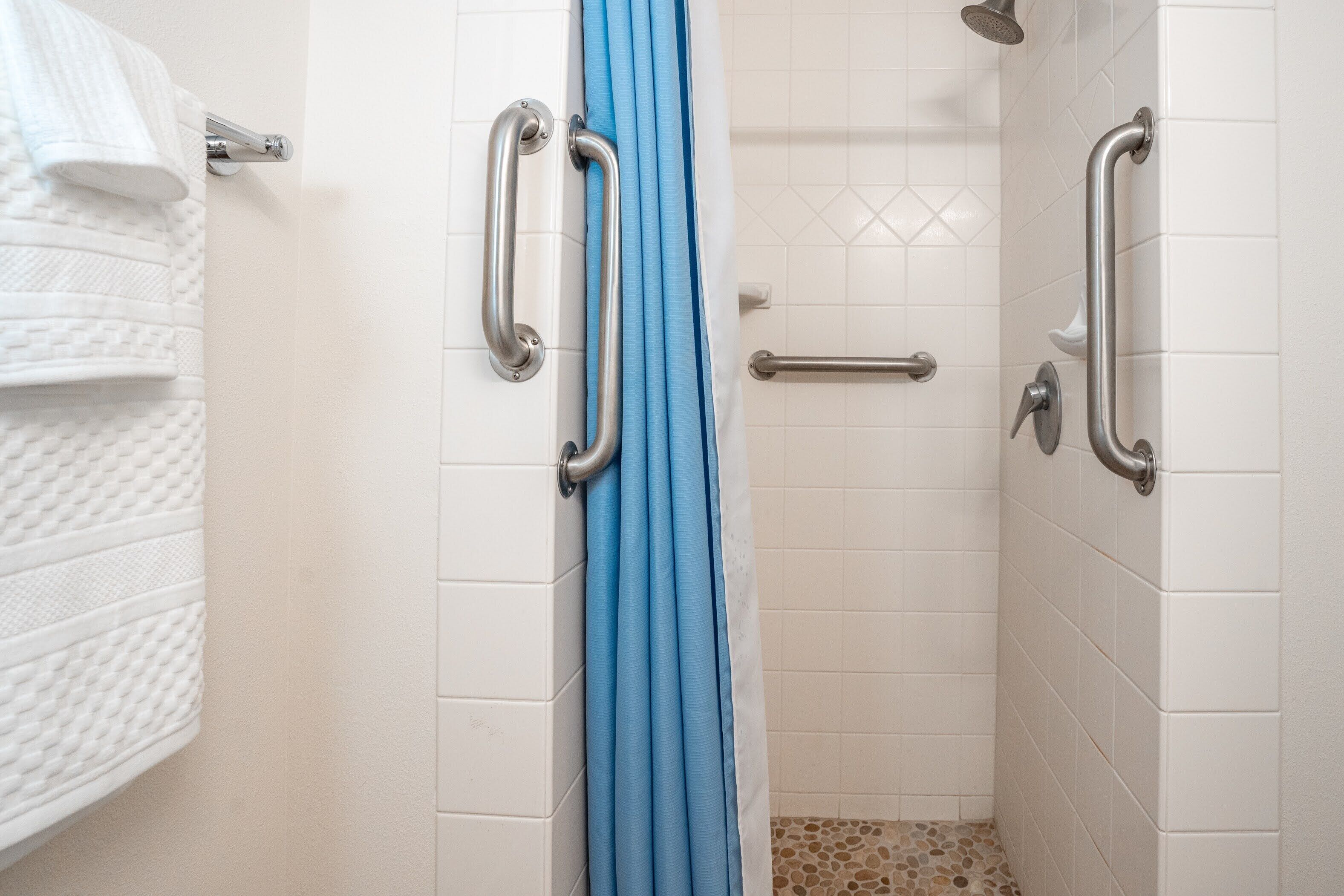 A bathroom with white tiled walls, a blue shower curtain, and grab bars.