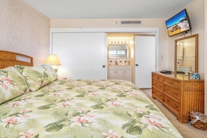A bedroom with a bed, a dresser, a mirror, and a television.