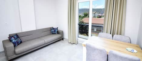 Ein modernes Wohnzimmer mit einer Couch, einem Esstisch mit Stühlen und einem großen Fenster mit Vorhängen.