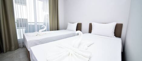 A hotel room with two beds, a large window with curtains, and a view of the outdoors.