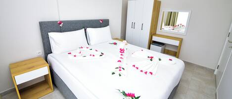 A neatly made bed with white linens and pink flower petals arranged on it.