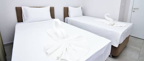 Two single beds with white linens and matching headboards, a white towel on the first bed, and a white robe on the second bed.