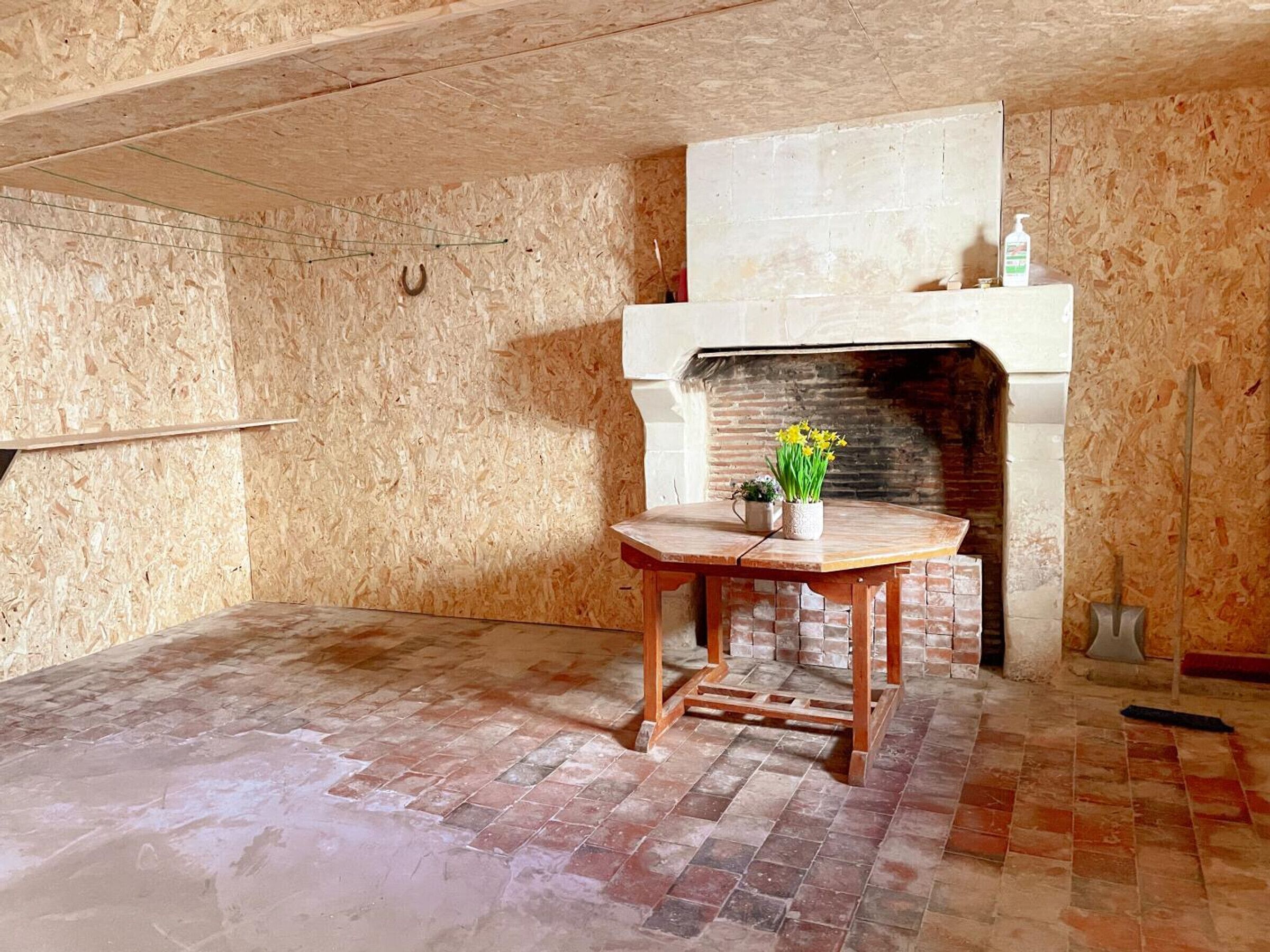 Een kamer met houten wanden, een open haard van baksteen en een kleine houten tafel met een bloemenvaas.