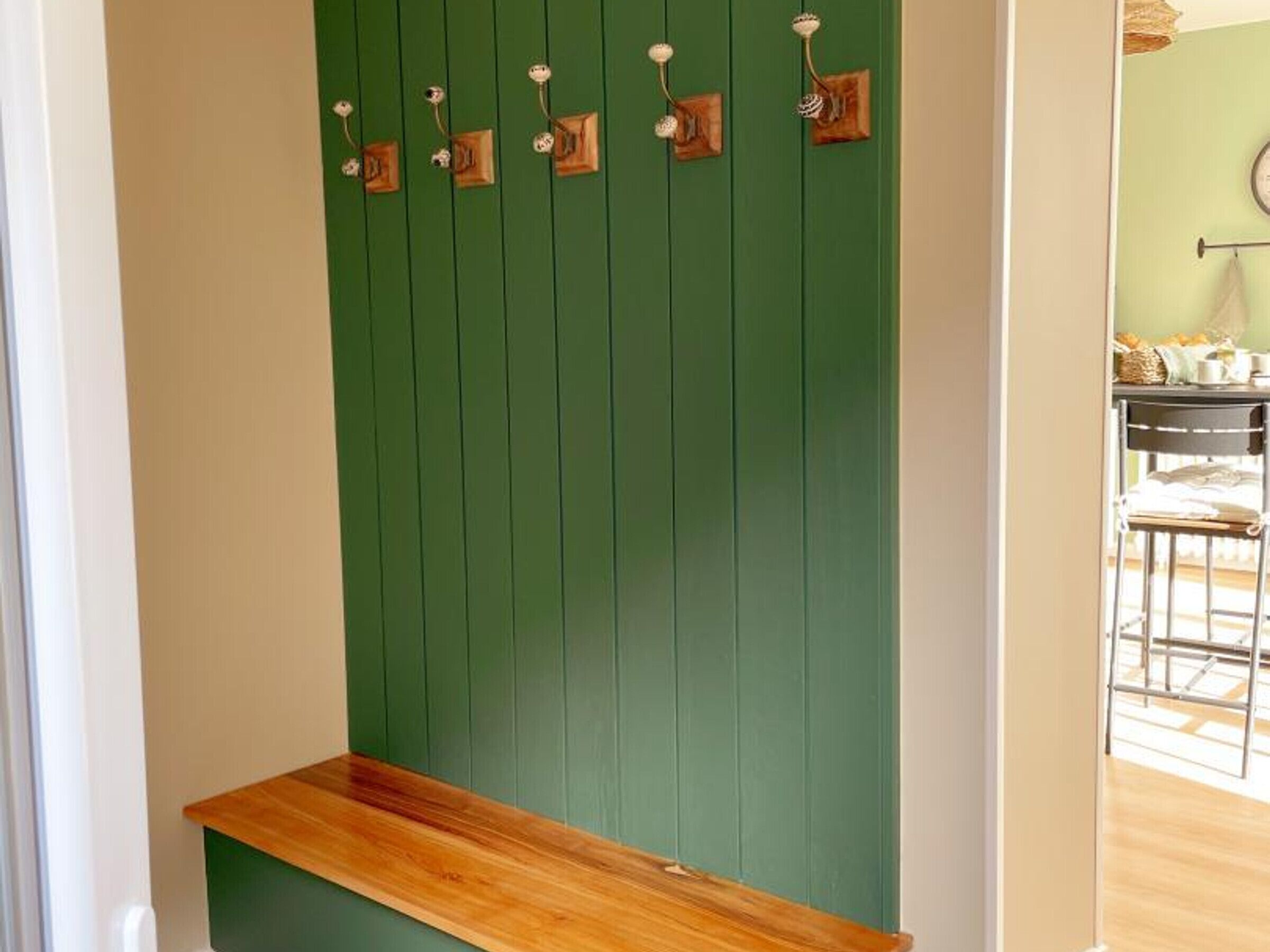 A green wall with wooden hooks and a wooden bench.