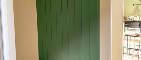 A green wall with wooden hooks and a wooden bench.