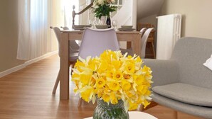 Un coin repas avec une table dressée pour deux personnes, un vase de fleurs jaunes et un escalier en arrière-plan.