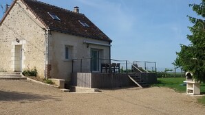 Un bâtiment à deux étages, doté d’un toit en pente, d’un petit porche avec des marches et offrant une vue sur la campagne.