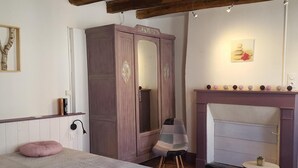 A bedroom with a bed, a wardrobe, a chair, a small table, and a fireplace.