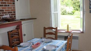 A dining area with a table set for four, wooden chairs, a window with a view of greenery, and a brick wall.