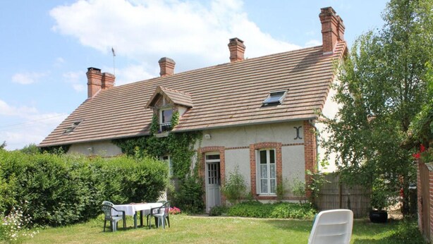 A house with a tiled roof, brick chimneys, and a garden with a lawn and a white chair.