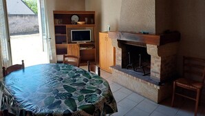 A cozy room with a wooden table, a television on a wooden shelf, and a fireplace. - Cozy house near Blois, pets allowed, parking (Chailles)