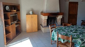 A room with a fireplace, wooden furniture, a television, and a table with a leaf-patterned tablecloth. - Cozy house near Blois, pets allowed, parking (Chailles)
